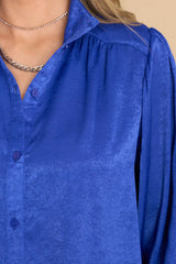 Close  up view of this top that features a collared neckline, functional blue buttons down the bodice, and balloon sleeves.