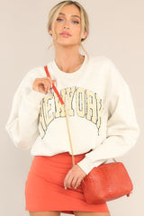 This oatmeal colored sweatshirt features a crew neckline, a textured city name, and cuffed long sleeves.