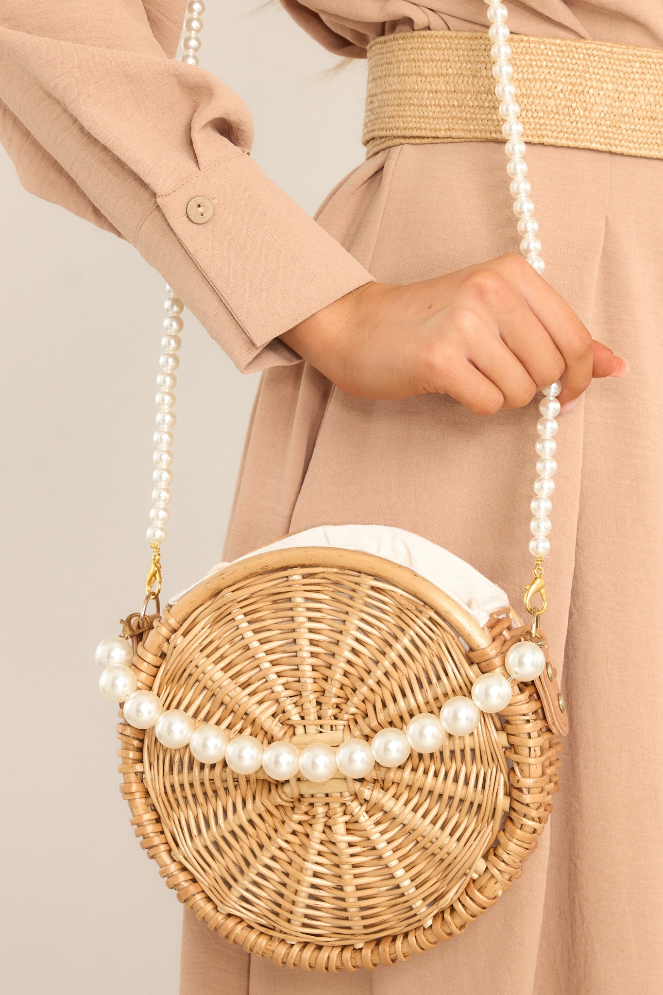 Front view of this handbag that features gold hardware, 2 removable faux pearl straps, a circular shape, and a drawstring closure.
