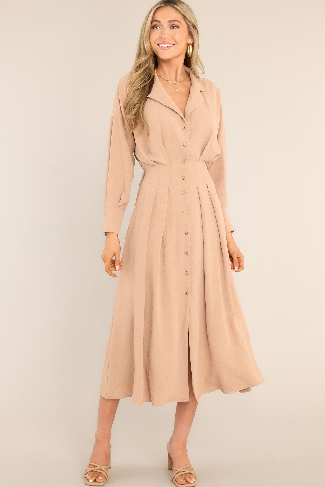 Full body view of this dress that features a collard neckline, functional buttons going down the front, long sleeves with button closures, and a pleated design at the waist.