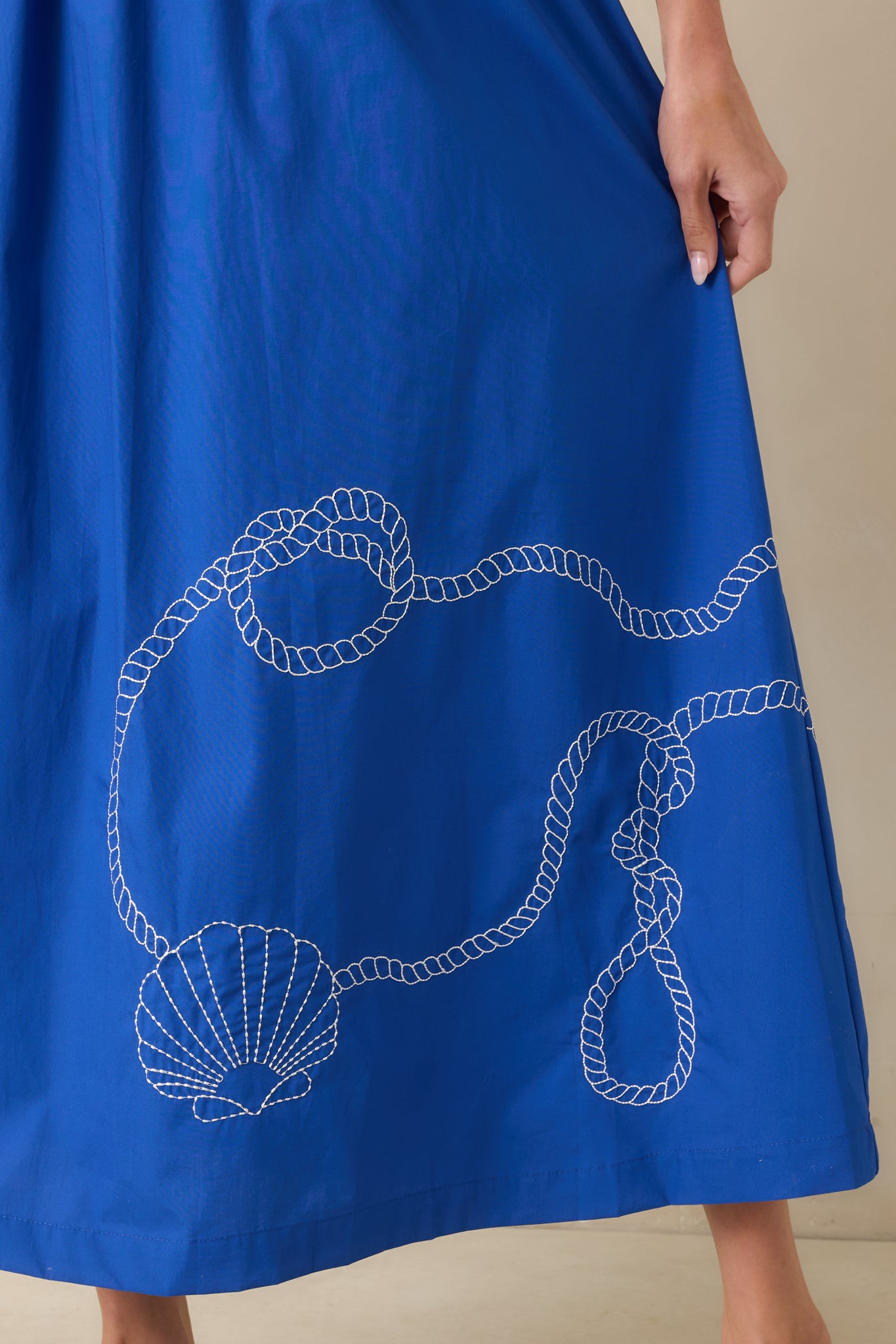 Close-up of the royal blue midi dress hem showcasing embroidered rope-inspired trim, shell motif accents, and intricate border detailing along the bottom edge.