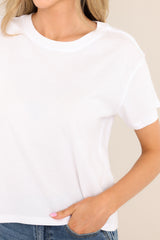 Close up view of a white tee featuring a ribbed crew neckline, a relaxed fit, and short sleeves.