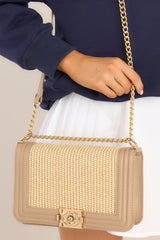 Close up view of this bag that features a single flap, a push lock closure, a shoulder length chain strap, natural woven fabric, and a small zipper pocket inside.