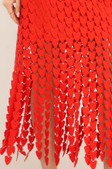 Close up view of this midi dress that features a playful red heart lace overlay and has a tassel like flow at the bottom and a lining that stops around the upper thigh.