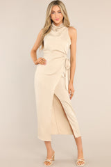 This beige dress features a high cowl neckline, a zipper down the back, a wrap-like design with a self-tie feature at the waist, and a front slit. 