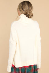 Back view of this sweater that features a very light eyelash knit design, a turtle cowl neckline, extremely dropped shoulders, and a slight high low hemline.