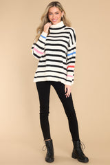 This ivory multi-colored sweater features a turtleneck, an all-over striped pattern, side slits, and cuffed long sleeves.