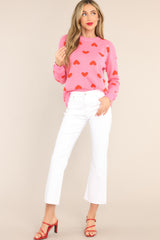 This pink and red sweater features a round ribbed neckline, ribbed cuffs, a lightweight style, and a fun heart pattern throughout.