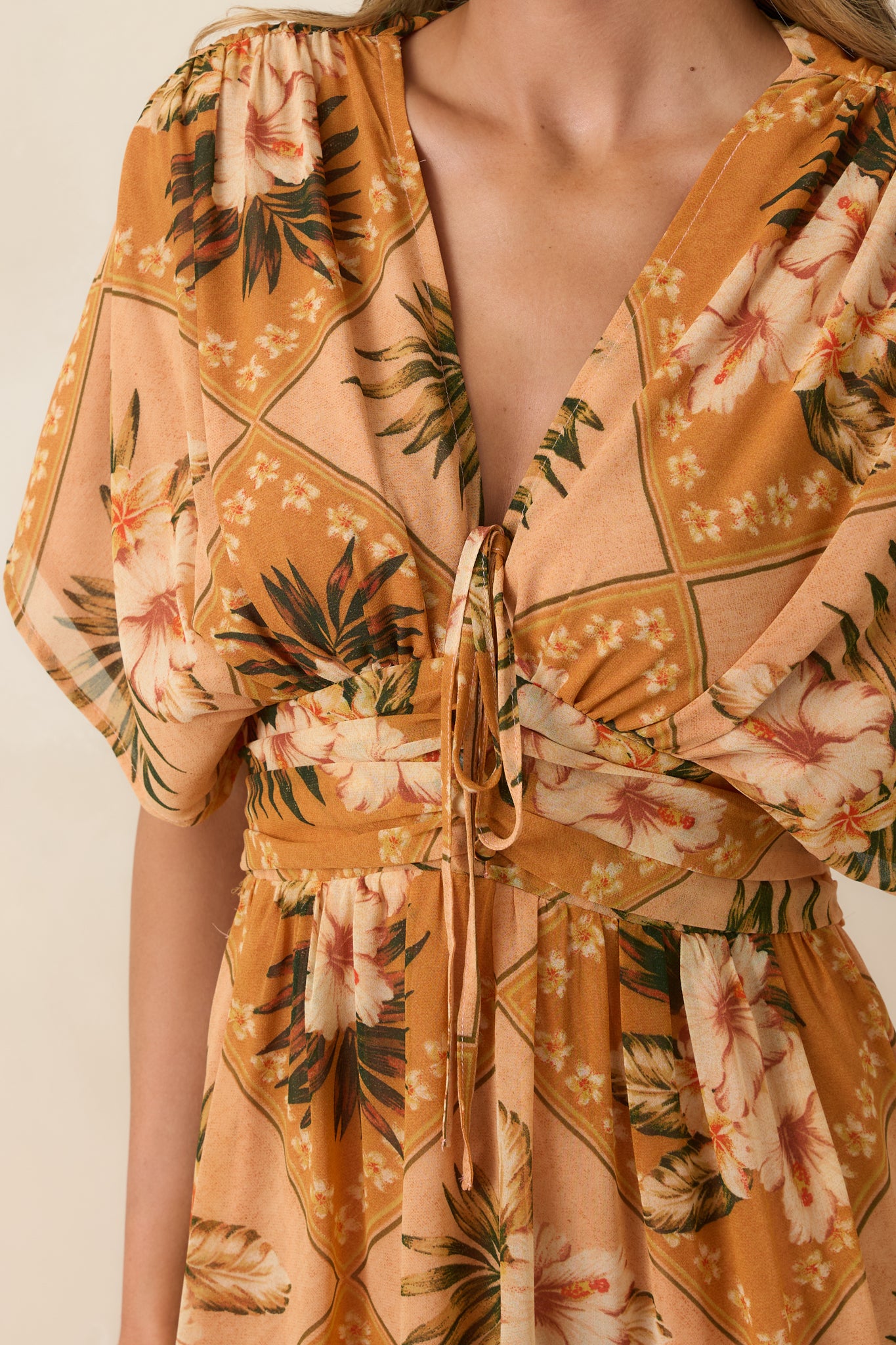 Close-up of peach tropical print fabric showing gathered bodice, front tie detail, and soft floral patchwork pattern.