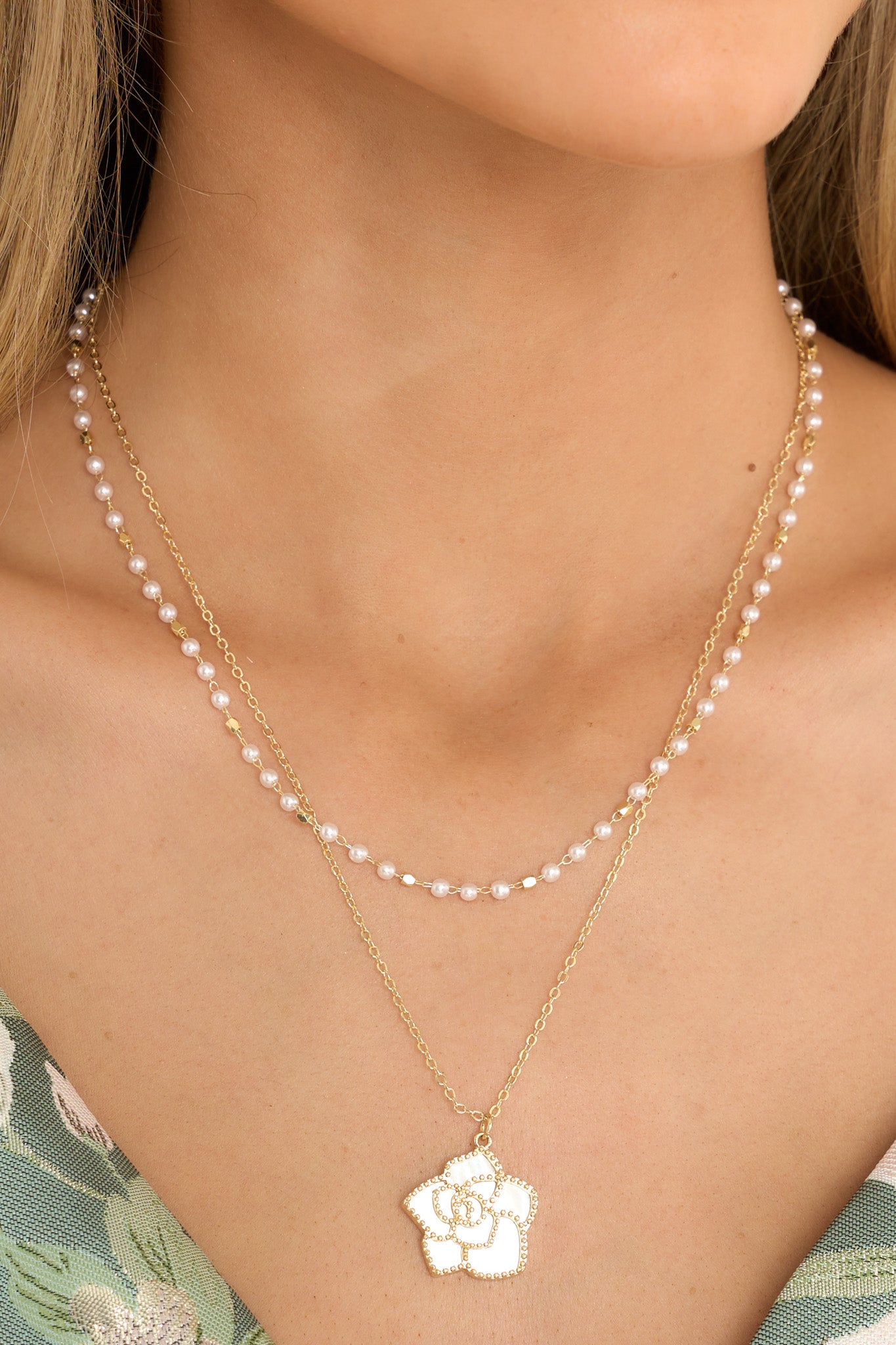 This gold and pearl necklace features gold hardware, a dainty faux pearl chain, a chain with an iridescent flower pendant, and a lobster claw closure. 