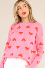 Front view of this sweater that features a round ribbed neckline, ribbed cuffs, a lightweight style, and a fun heart pattern throughout.