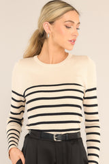 This beige and black top features a crew neckline, a stretchy ribbed fabric, a striped pattern, and long sleeves.