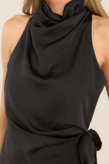 Close up view of this dress that features a high cowl neckline, a zipper down the back, a wrap-like design with a self-tie feature at the waist, and a front slit. 