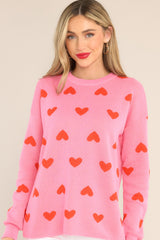 Front view of this sweater that showcases the red heart pattern of the pink fabric.