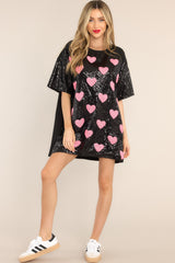 This black tunic features a round neckline, short sleeves, functional waist pockets, a jersey-style silhouette, colorful sequins throughout, and a fun heart pattern. 