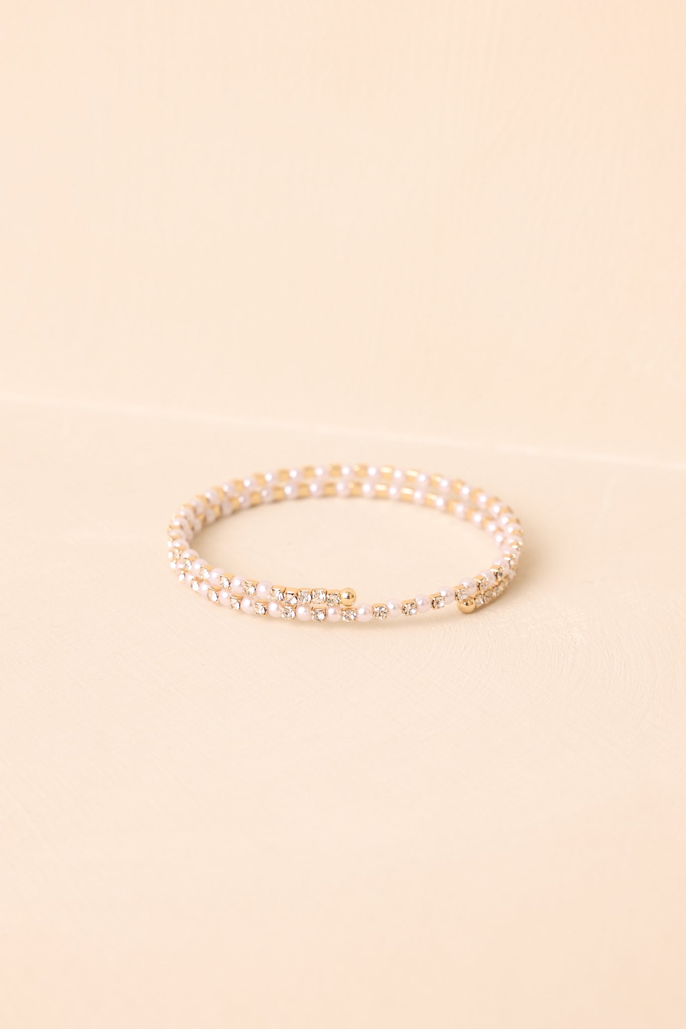 A cropped view of the double-row wrap bracelet with alternating ivory faux pearls and clear rhinestones in a gold-tone base.