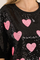 Close up view of this tunic that features a round neckline, short sleeves, functional waist pockets, a jersey-style silhouette, colorful sequins throughout, and a fun heart pattern. 