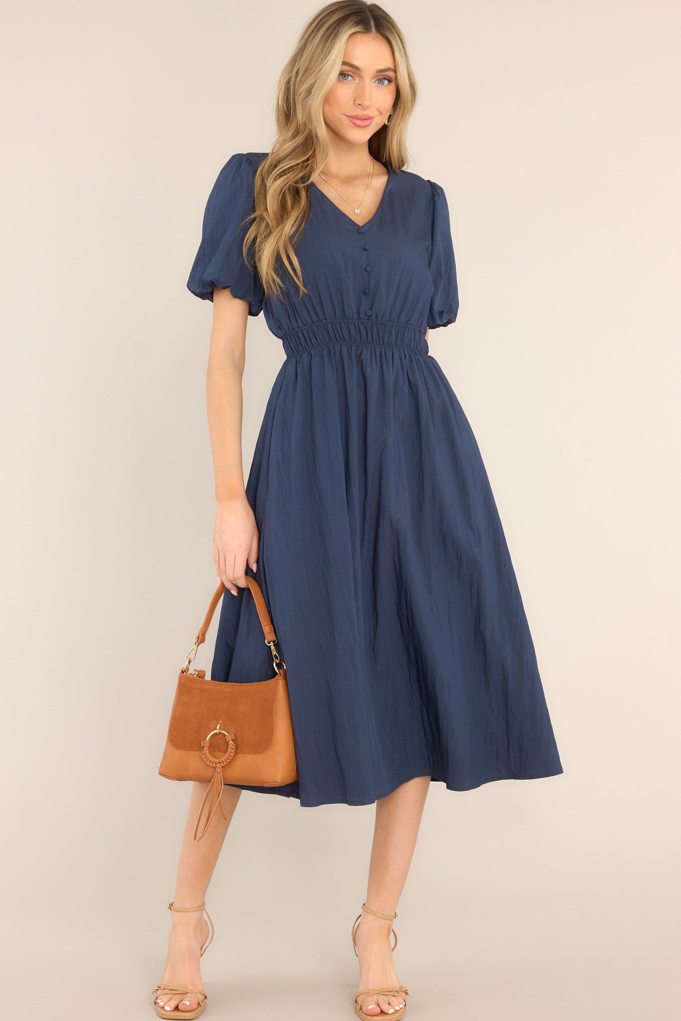 This all navy blue dress is featuring elastic short sleeves, an elastic waist, a keyhole opening in the back, non-functional buttons down the bust, and a midi length.