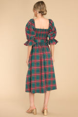 Back view of this dress that features a square neckline, a fully smocked bust, a self-tie waist belt, functional pockets, elastic cuffed sleeves, and an all over plaid print. 