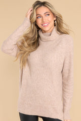 This light brown sweater features a cowl turtle neckline, long sleeves with ribbed cuffs, and a bottom hem that tapers in around the hips.