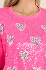 Close up view of this tunic that features a round neckline, short sleeves, functional waist pockets, a jersey-style silhouette, colorful sequins throughout, and a fun heart pattern. 