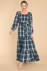 This forest green dress features a square neckline, long sleeves with elastic cuffs, a fully smocked bust section, a self-tie belt at the waist, a long flowy skirt, and a blue and white plaid pattern.