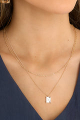 This gold necklace features a twisted chain, a chain with a rhinestone pendant, and a lobster claw clasp. 