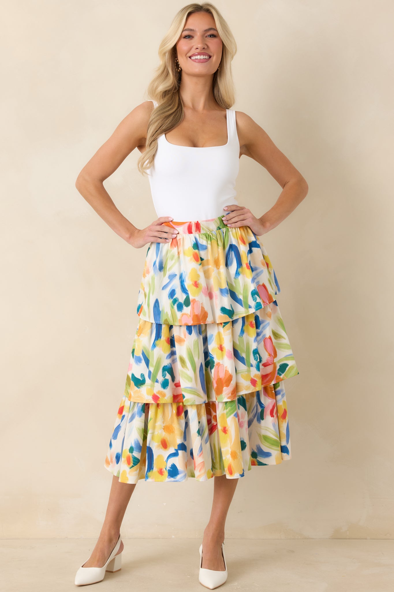 Woman wearing a colorful tiered midi skirt with a white top against a beige background.