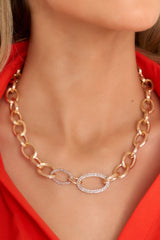 This gold necklace features gold hardware, large oval links, delicate rhinestone detailing, and a lobster claw closure. 