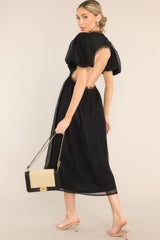 This all black midi dress features a round tulle neckline, short puff sleeves, an open back with a four button closure, and a tulle flowy skirt. 