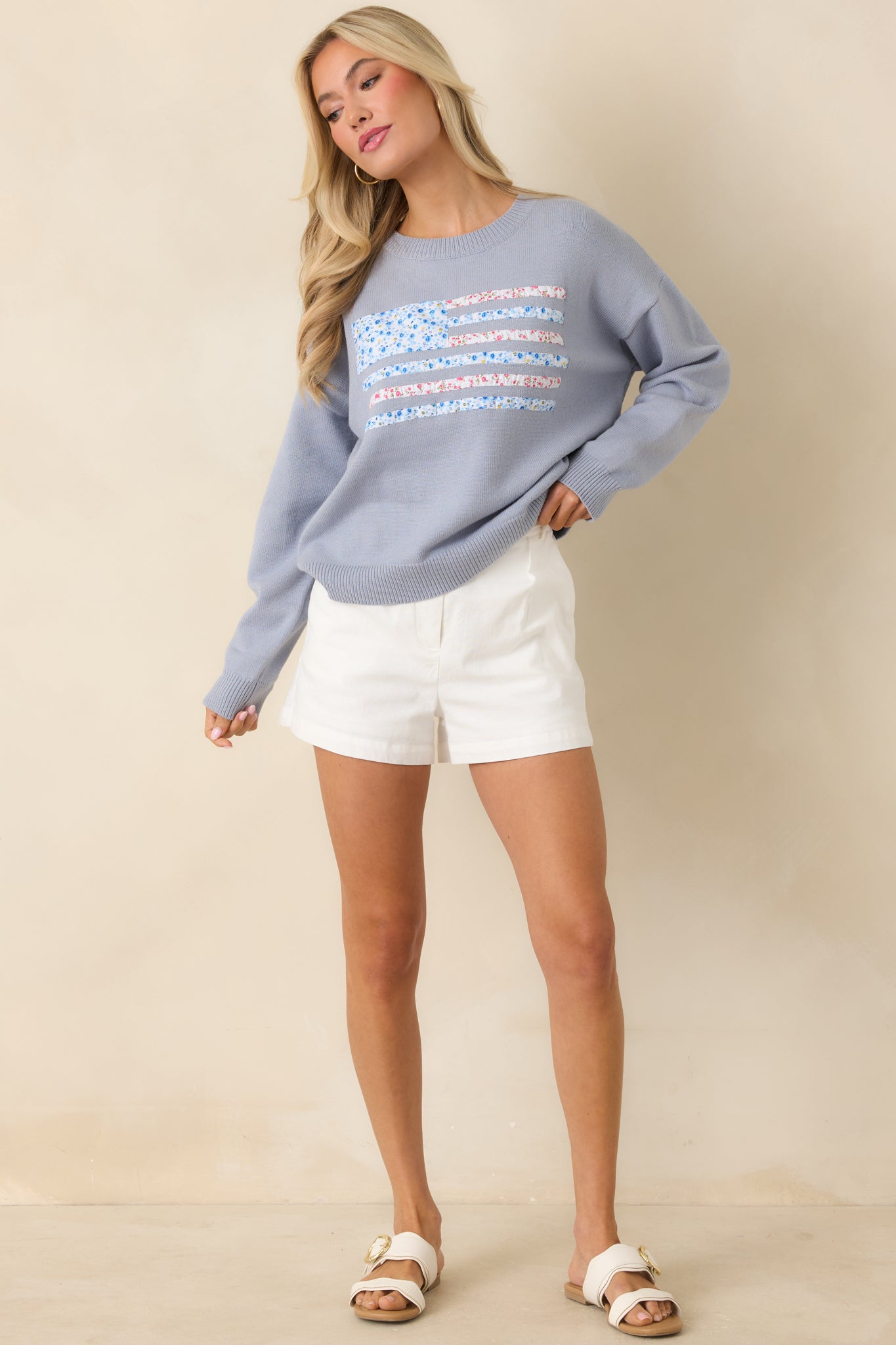 Woman wearing a light blue sweater with a textured patchwork and alternating floral pattern.
