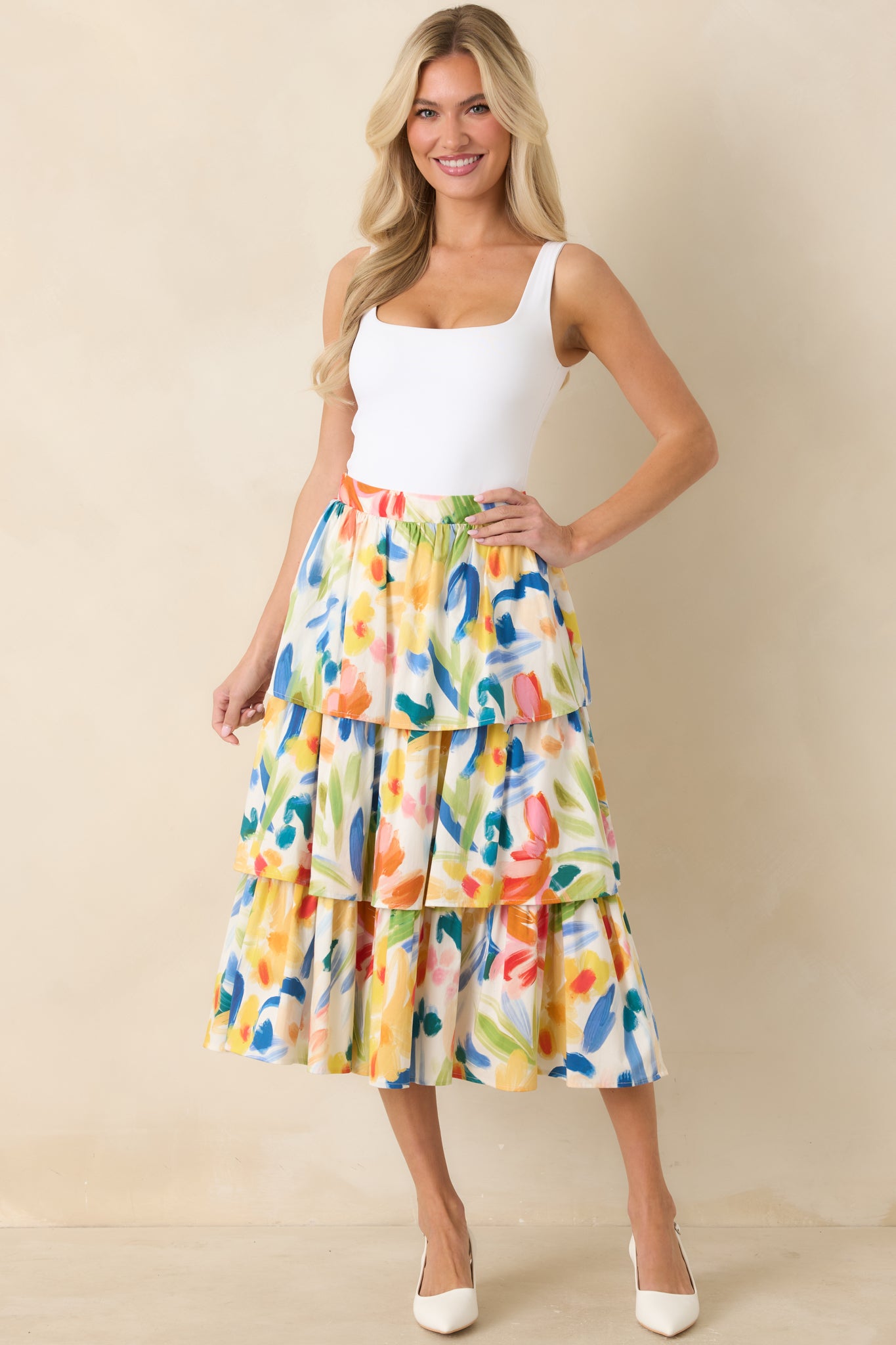 Woman wearing a colorful floral skirt and white top on a beige background.