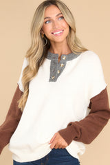 This earth toned sweater features a round neckline with a functional four button closure in the front, long sleeves with tapered cuffs, and a neutral colorblock pattern. 