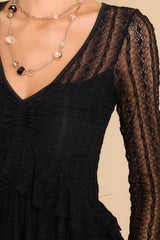 Close up view of this dress that features detailed lace fabric throughout, a v-neckline, and sheer long sleeves. 
