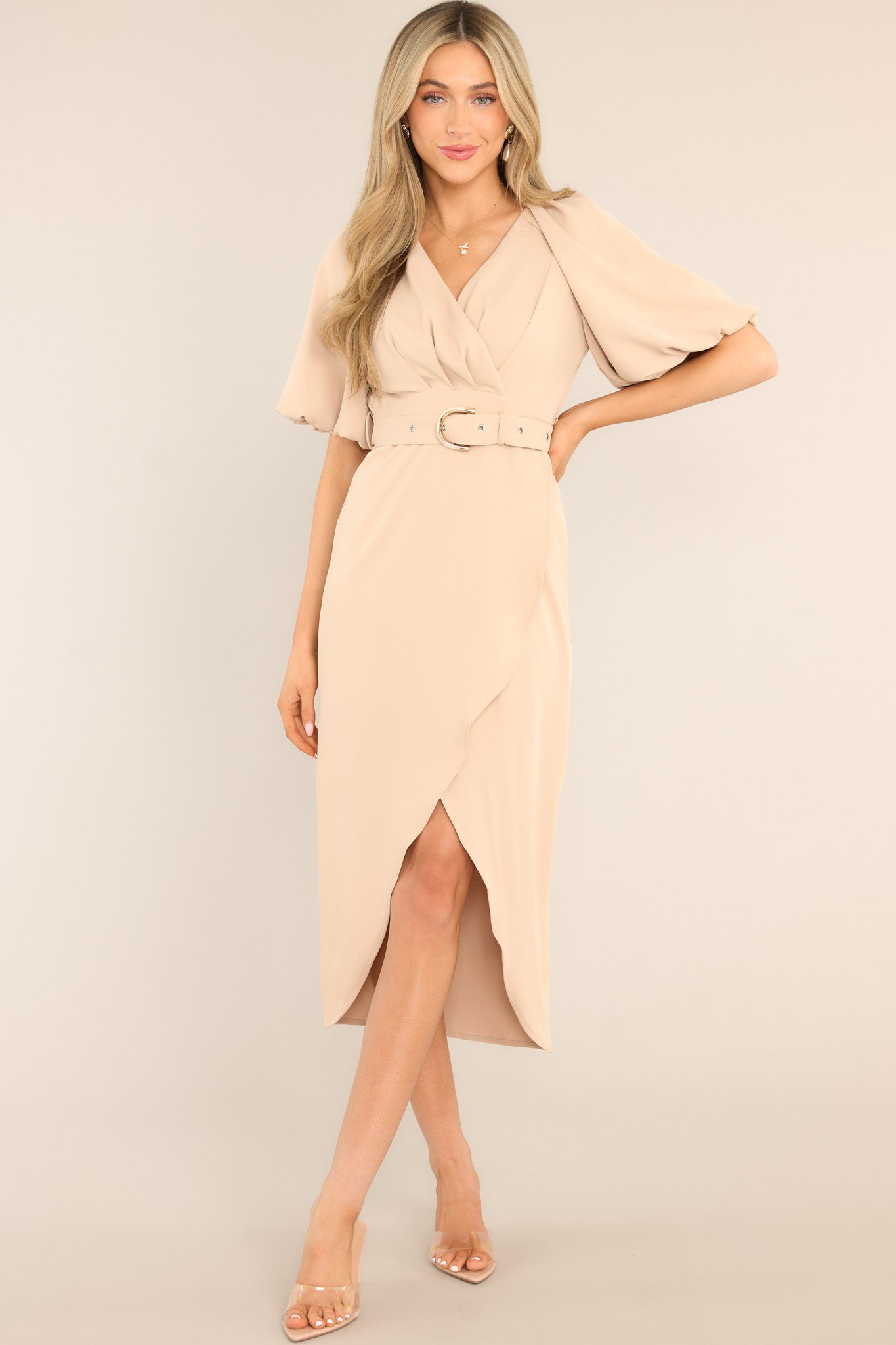 Full body view of this dress that features a v-neckline, a zipper down the back, belt loops, a functional belt, an asymmetrical hemline, and elastic cuffed sleeves.