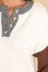 Close up view of this sweater that features a round neckline with a functional four button closure in the front, long sleeves with tapered cuffs, and a neutral colorblock pattern.