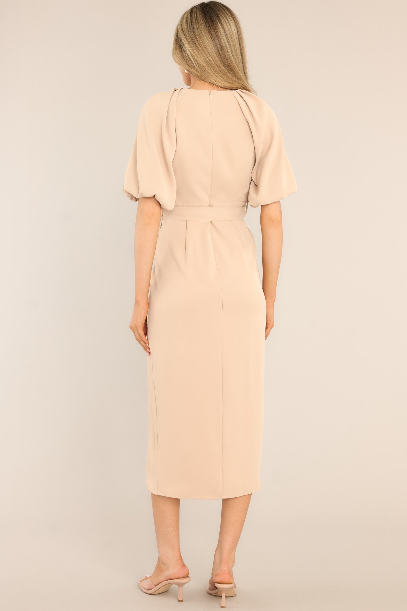 Back view of this dress that features a v-neckline, a zipper down the back, belt loops, a functional belt, an asymmetrical hemline, and elastic cuffed sleeves.