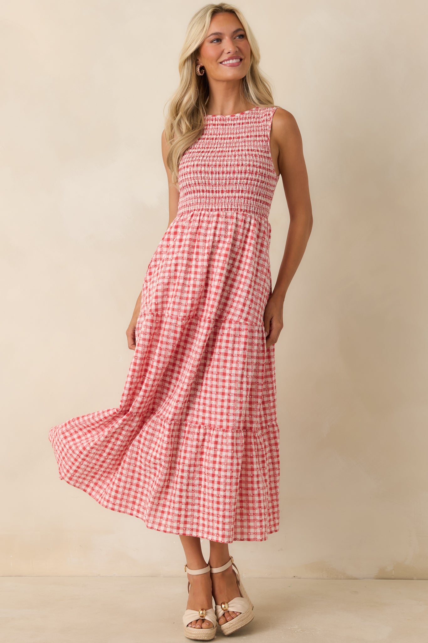 Red gingham midi dress featuring a sleeveless silhouette, full smocked bust, and tiered skirt.