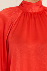 Close up view of this top that features a high neckline, balloon sleeves with buttons at the cuff, an adjustable self tie around the neck, and a flowy fit.