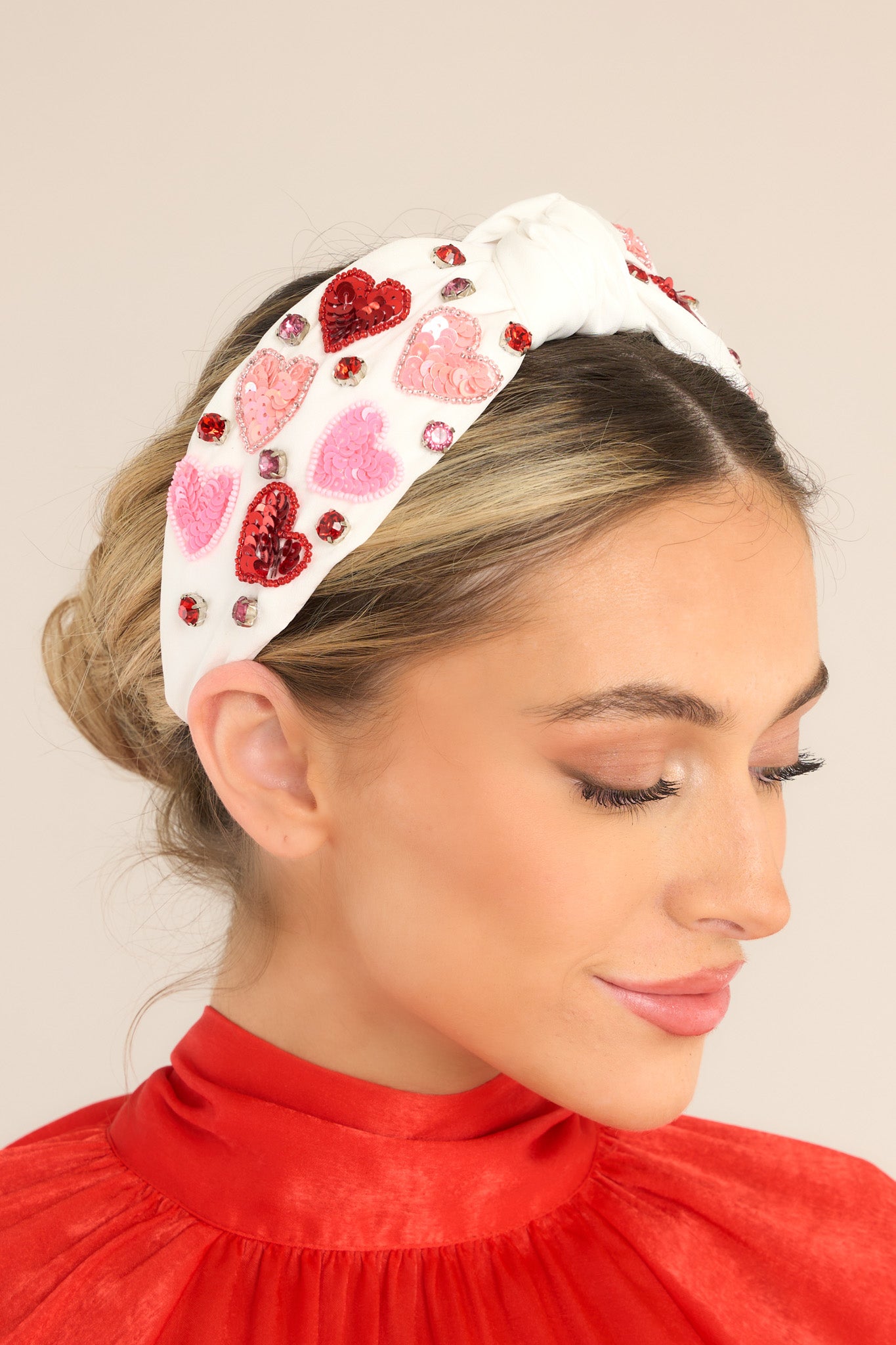 This white headband features sequin hearts and rhinestone detailing, and a knot detail. 
