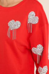Close up view of this sweatshirt that features silver rhinestone hearts, silver tassels, and ribbed hemming. 