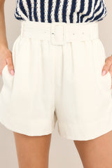Close up view of these shorts that feature a high waisted design, an elastic waistband, a square buckle fabric belt, belt loops, and functional pockets.