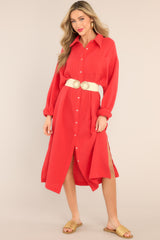This red dress features a collared neckline, functional buttons down the front, a front pocket on the left side of the bust, long sleeves with a cuff secured by a functional button, and two slits up the bottom hemline ending just below the knee.