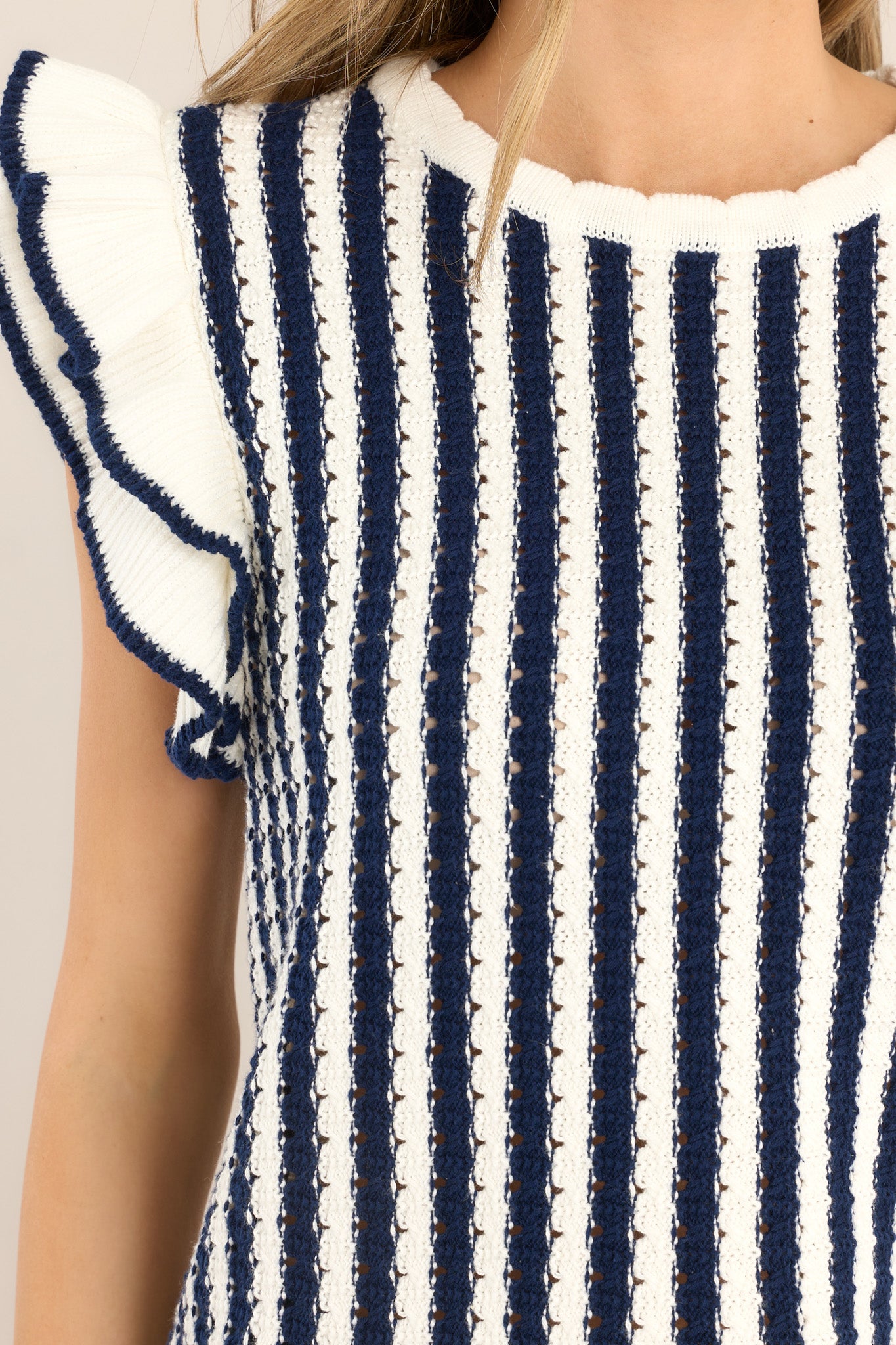 Close up view of this top that features a crew neckline, a vertical striped pattern, flutter sleeves, and a slightly scalloped hemline. 