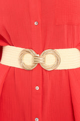 This beige belt features a circular double buckle, a hook and eye closure, a soft stretchy exterior, and gold hardware.