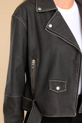 Close up view of this jacket that features a double breasted collar, zipper closure, zippered pockets, and attached waist belt with buckle closure.