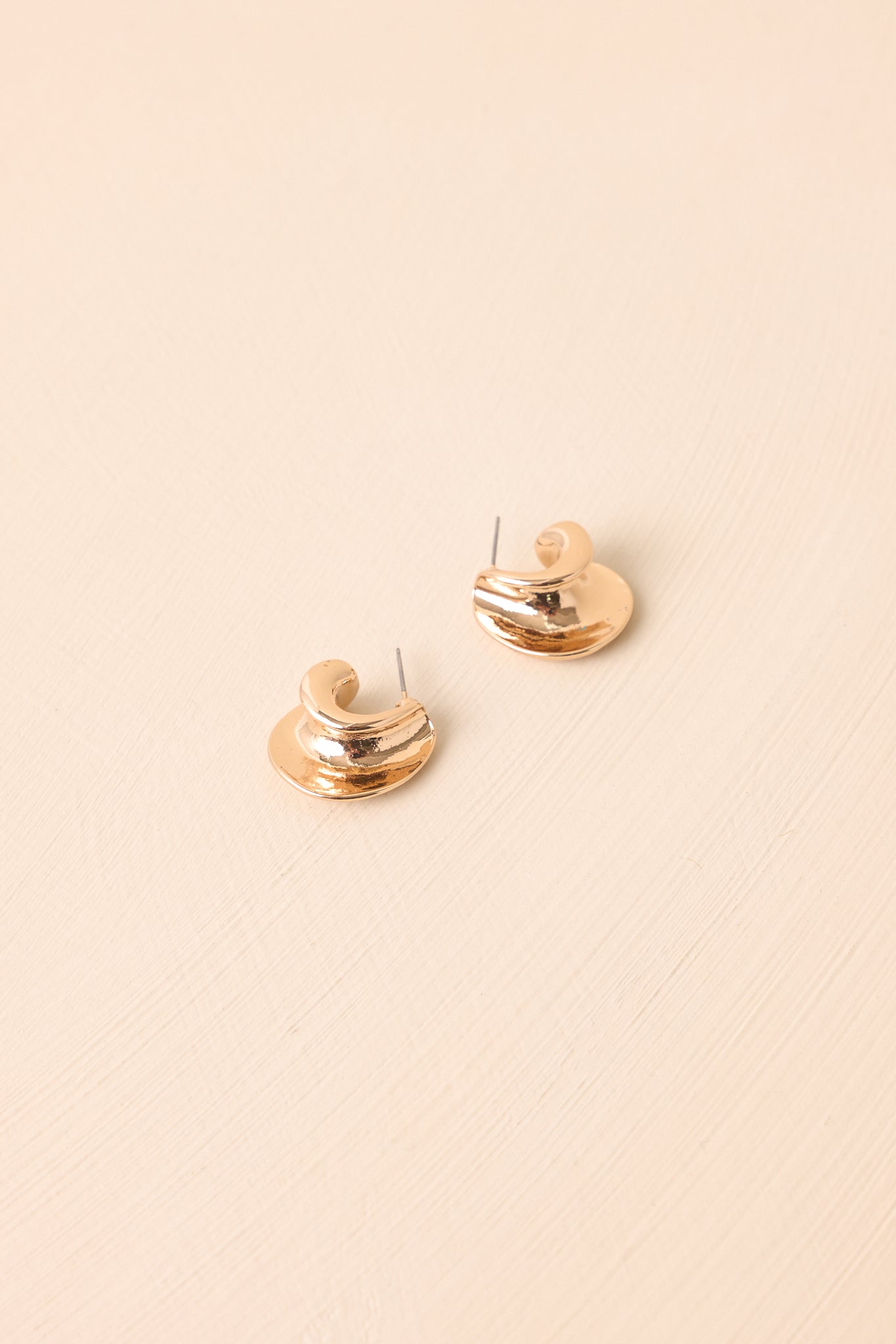 A pair of gold hollow c-hoop earrings displayed on a beige background with a shiny surface.