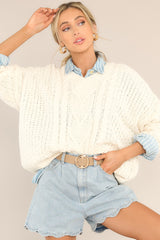 This ivory sweater features a ribbed v-neckline, long sleeves with ribbed cuffs, a bottom hem that tapers in, and a chunky knit design throughout.