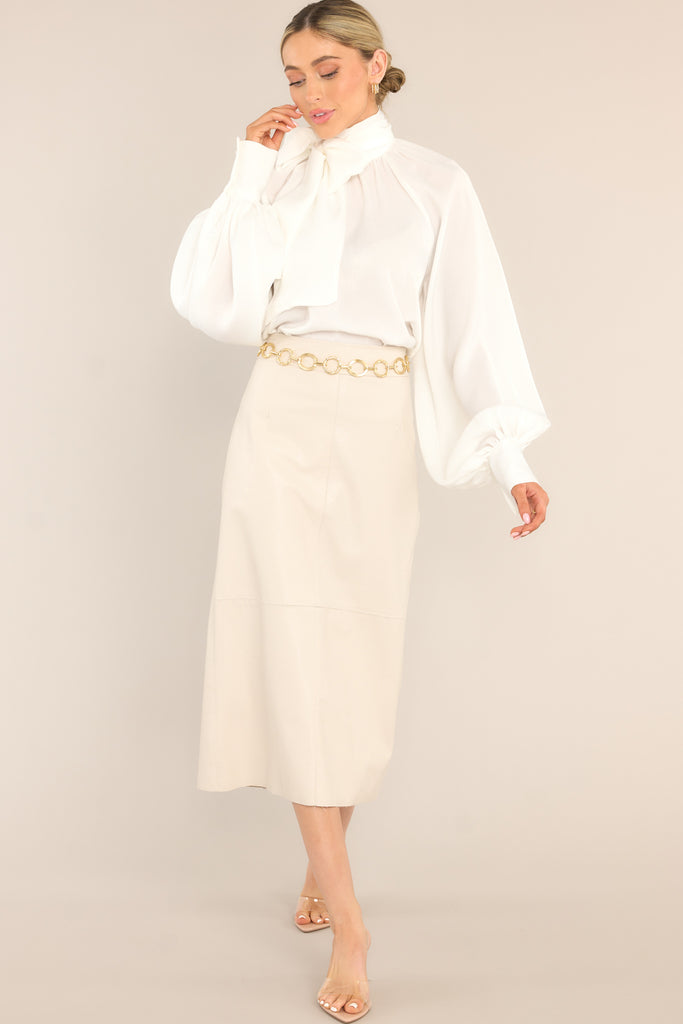 This white top features a high neckline, balloon sleeves with buttons at the cuff, an adjustable self tie around the neck, and a flowy fit.