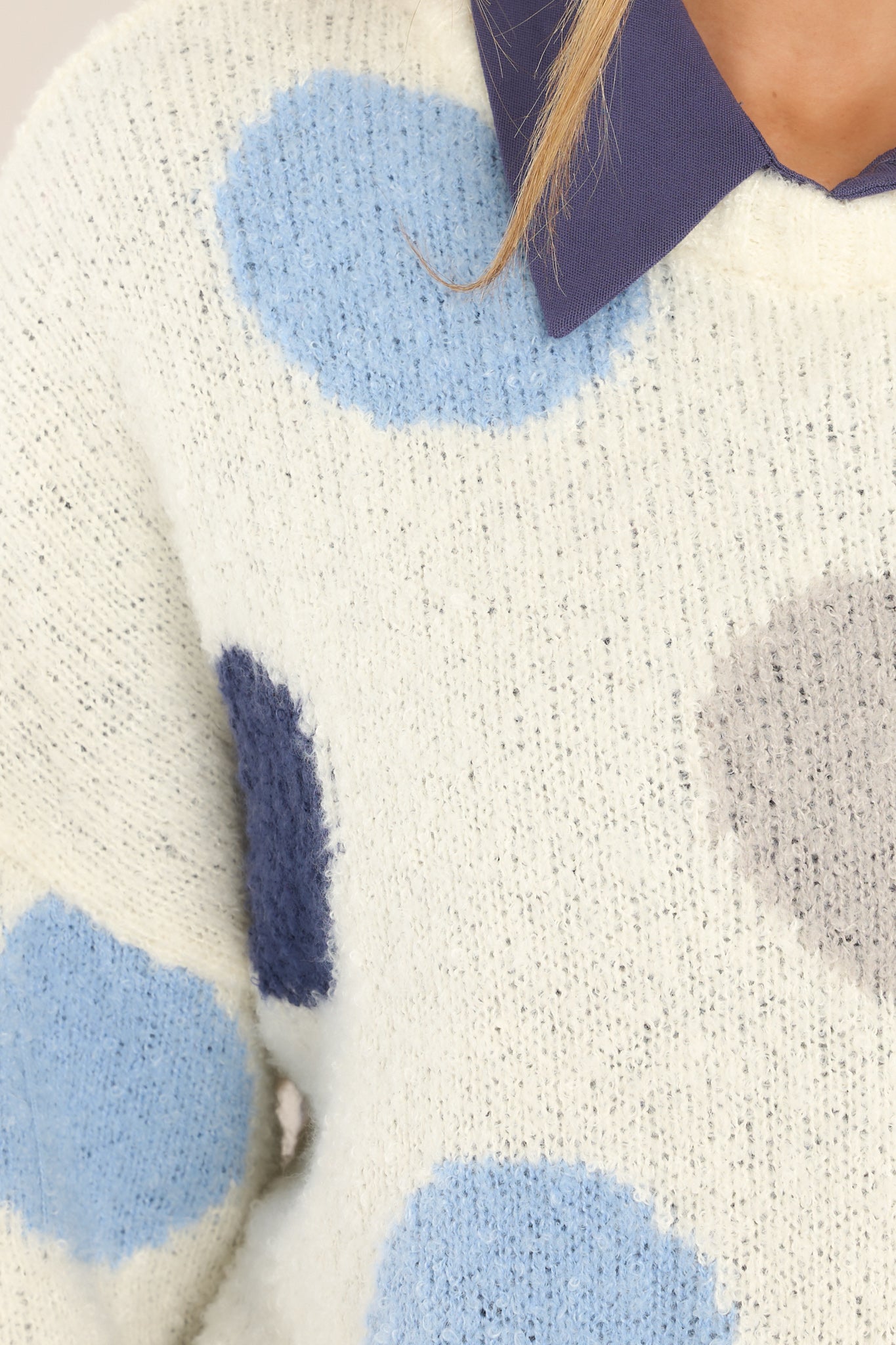 Close up view of this sweater that features a crew neckline, dropped shoulders, a blue polka dot design, ribbed cuffed sleeves and a ribbed hemline.